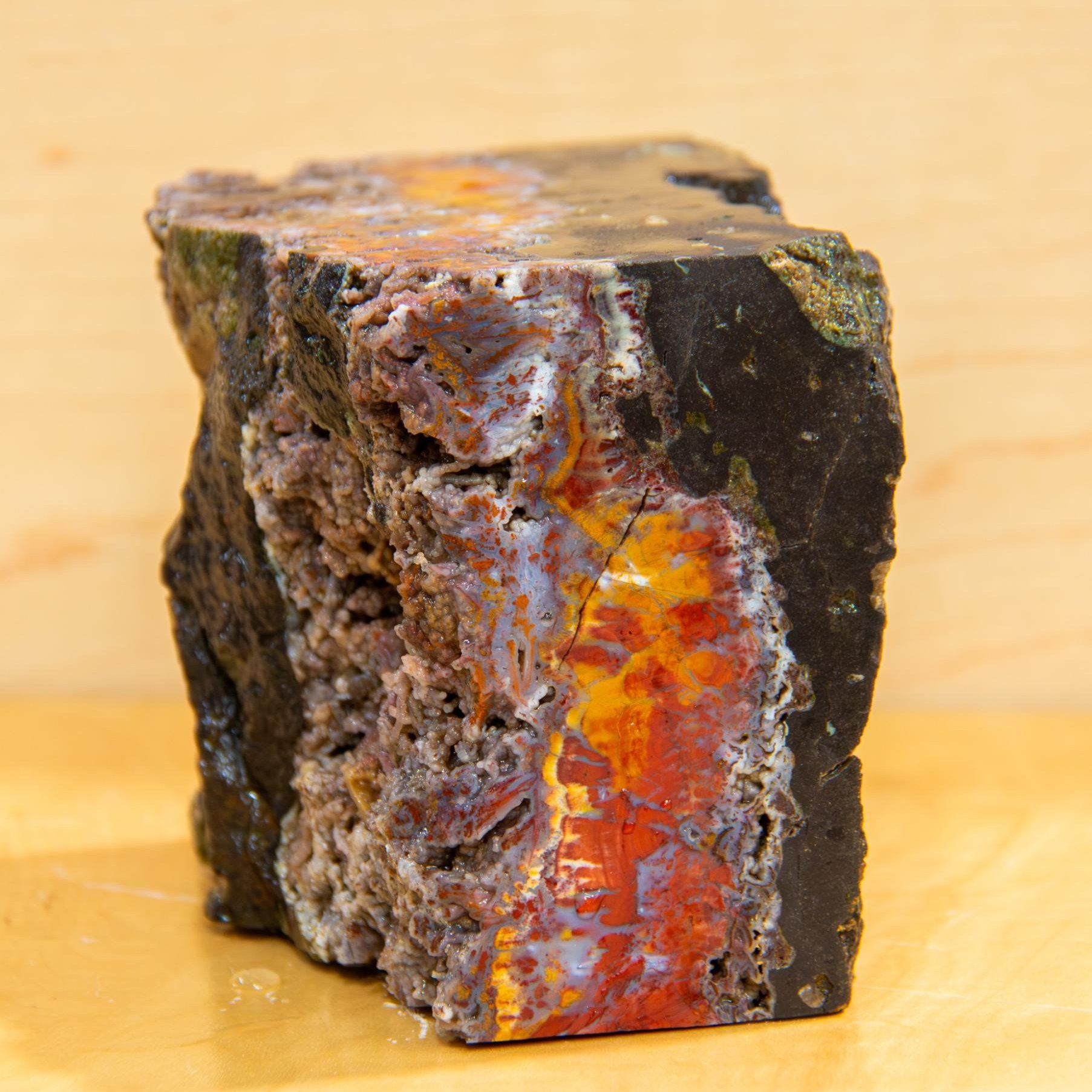 A rough stone with a polished cut face, a seam of red and orange running through dark rock.